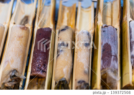 Closeup of sticky rice rolls grilled in bamboo tubes showing traditional street food texture smoky flavor natural cooking method Closeup of sticky rice rolls grilled in bamboo tubes showing traditional street food texture smoky flavor natural cooking method 139372508