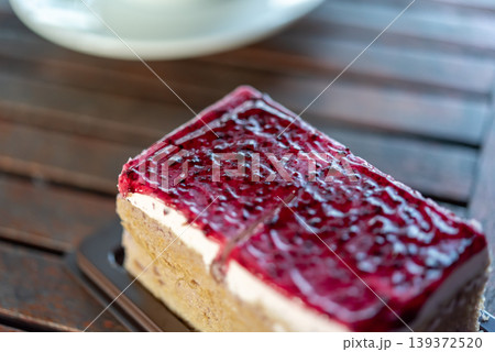 Closeup of cheesecake slice topped with glossy berry sauce on wooden table creamy texture sweet dessert bakery treat rich flavor Closeup of cheesecake slice topped with glossy berry sauce on wooden table creamy texture sweet dessert bakery treat rich flavor 139372520
