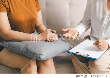 Close up of patient holding hands on pillow while therapist gestures with clipboard during mental health counseling session, symbolizing communication, support, trust, guidance and care. Close up of patient holding hands on pillow while therapist gestures with clipboard during mental health counseling session, symbolizing communication, support, trust, guidance and care. 139373384
