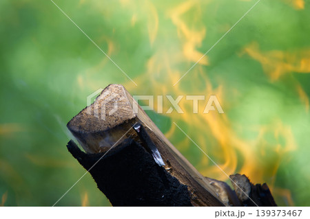 Close-up of burning wood logs with vibrant orange flames against a green background 139373467