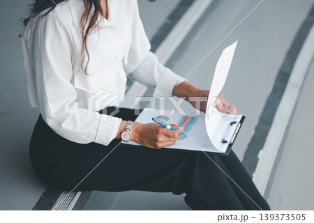 Close-up of a businesswoman reviewing charts and report pages on a clipboard, ideal for data analysis, financial reporting, office administration, audit, planning, and workflow concepts. Close-up of a businesswoman reviewing charts and report pages on a clipboard, ideal for data analysis, financial reporting, office administration, audit, planning, and workflow concepts. 139373505