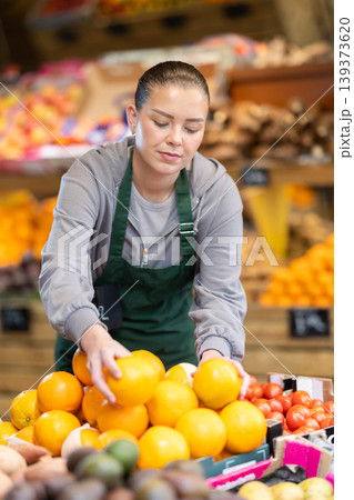 Young woman seller puts oranges in store Young woman seller puts oranges in store 139373620
