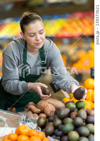 Fruit shop worker checking quality premium avocado on shelf Fruit shop worker checking quality premium avocado on shelf 139373621