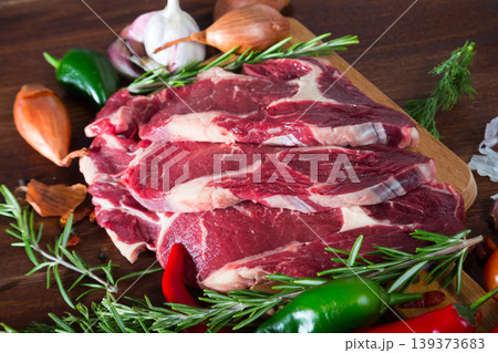 Raw beef steaks with rosemary and vegetables assortment on wooden desk Raw beef steaks with rosemary and vegetables assortment on wooden desk 139373683
