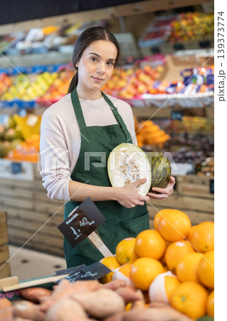 Young woman seller puts melon in store Young woman seller puts melon in store 139373774