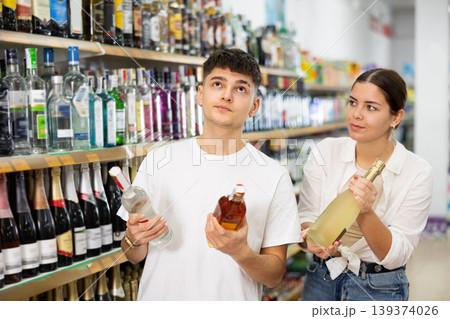Young couple of customer diligently picking out bottle of liquor Young couple of customer diligently picking out bottle of liquor 139374026