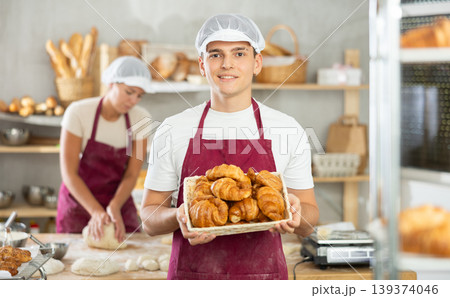 Young male baker holding croissants in square wicker basket Young male baker holding croissants in square wicker basket 139374046
