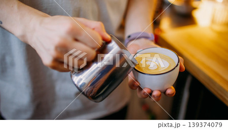 Latte art. Coffee shop. Male barista hand pouring milk from metal pitcher to cup making heart shape pattern on drink in cafeteria. Latte art. Coffee shop. Male barista hand pouring milk from metal pitcher to cup making heart shape pattern on drink in cafeteria. 139374079
