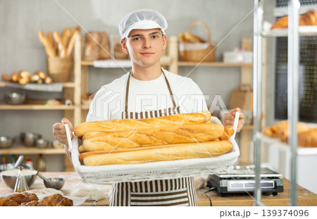 Young male baker holding baguettes in wicker basket 139374096