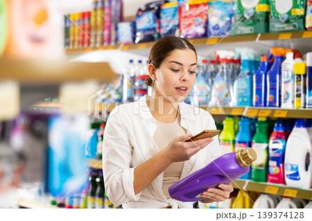 Young woman looking up laundry detergent contents on internet in supermarket Young woman looking up laundry detergent contents on internet in supermarket 139374128