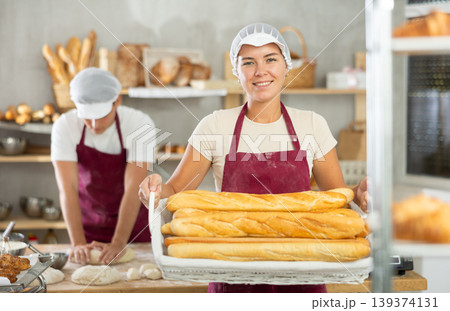 Young female baker holding baguettes in wicker basket Young female baker holding baguettes in wicker basket 139374131