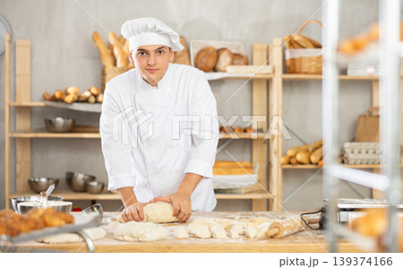 Working in bakery - guy kneads raw dough to make baguettes or croissants 139374166