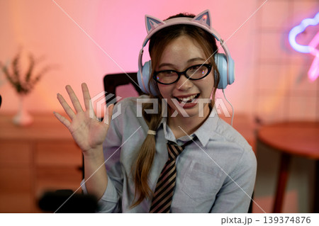 Asian adult woman waving smiling wearing cat ear headphones streaming gaming from home studio happy female content creator greeting viewers Asian adult woman waving smiling wearing cat ear headphones streaming gaming from home studio happy female content creator greeting viewers 139374876