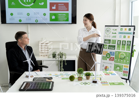 Asian business woman presenting solar panel future energy to male executive sustainable development corporate responsibility green initiatives environment solutions meeting room 139375016