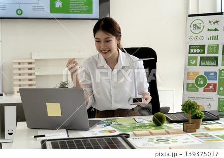 Asian adult woman celebrates renewable energy project success working on net zero carbon reduction green business strategy in office environment sustainability meeting 139375017