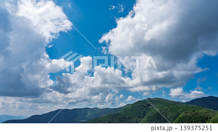 真夏の青空に流れるたくさんの白い雲と、緑に包まれた山々 139375251