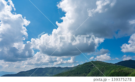 真夏の青空に流れるたくさんの白い雲と、緑に包まれた山々 139375278