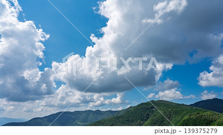 真夏の青空に流れるたくさんの白い雲と、緑に包まれた山々 139375279