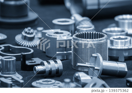 Group of high precision metal parts and components manufactured by CNC lathe machine in a blue-toned industrial setting. Group of high precision metal parts and components manufactured by CNC lathe machine in a blue-toned industrial setting. 139375362