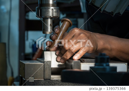 Professional machine operator setting up metal workpieces on an NC milling machine using a copper hammer for precision adjustment. Professional machine operator setting up metal workpieces on an NC milling machine using a copper hammer for precision adjustment. 139375366