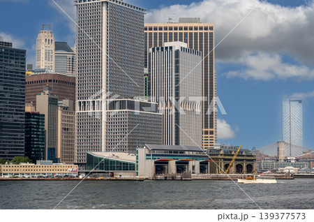 New york, usa august 16,2024. New york city skyline with financial district skyscrapers and staten island ferry terminal building, a boat traveling on the water 139377573