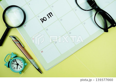 Do it! message written on calendar date with alarm clock, glasses and magnifying glass on yellow background 139377660