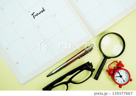 Travel message written on calendar date with alarm clock, glasses and magnifying glass on yellow background Travel message written on calendar date with alarm clock, glasses and magnifying glass on yellow background 139377667