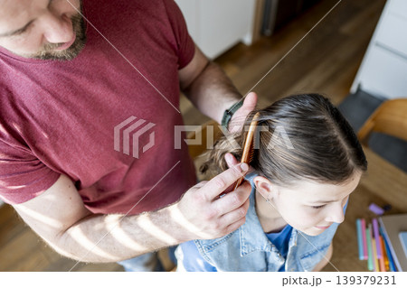 Dad brushing daughter hair and making braid at home. Dad brushing daughter hair and making braid at home. 139379231