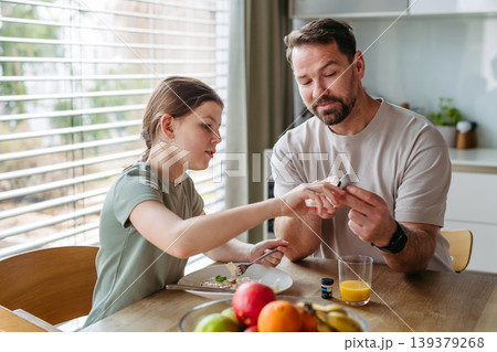 Father checking blood sugar level of diabetic teenage daughter using glucose meter. 139379268
