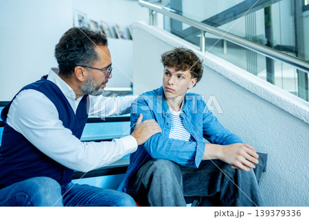 Teacher talking with struggling student, sitting on stairs in school hallway. Teacher talking with struggling student, sitting on stairs in school hallway. 139379336