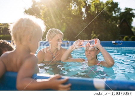 Young family with two children in swimming pool outdoors in backyard garden. 139379387