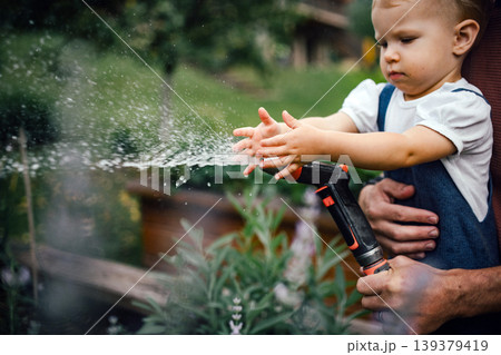 Close up of kid playing and watering plants with hose. 139379419