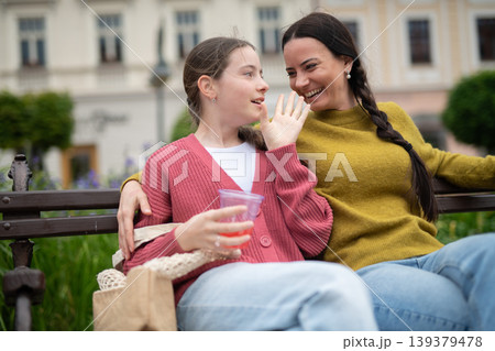 Mother and daughter sitting on park bench, talking. 139379478
