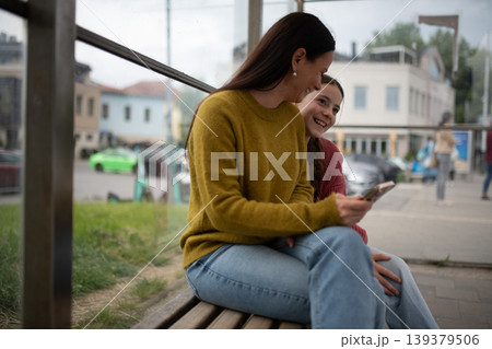 Woman and teenage girl waiting at bus stop. Woman and teenage girl waiting at bus stop. 139379506