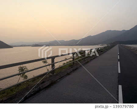 Scenic reservoir causeway at dusk with distant mountains and calm water Scenic reservoir causeway at dusk with distant mountains and calm water 139379780