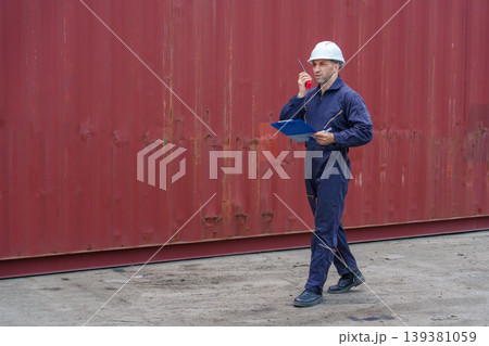 Mid-adult Caucasian male supervisor talking on walkie-talkie with clipboard at Asian shipping container harbor. Mid-adult Caucasian male supervisor talking on walkie-talkie with clipboard at Asian shipping container harbor. 139381059