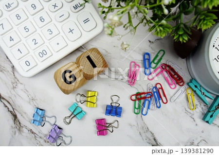 GI (Gross Income) alphabet letters with calculator and alarm clock on marble background GI (Gross Income) alphabet letters with calculator and alarm clock on marble background 139381290