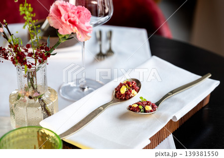 Spoons tartare on napkin beside flower, stemware and vase, plush red seating 139381550
