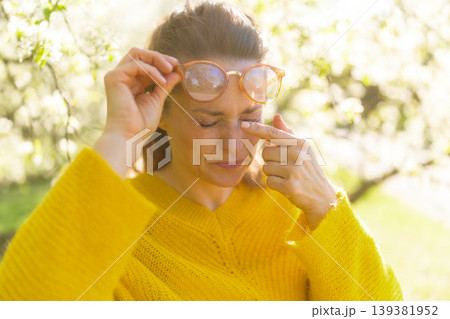 Woman Rubbing Irritated Eye in Sunny Spring Orchard Woman Rubbing Irritated Eye in Sunny Spring Orchard 139381952