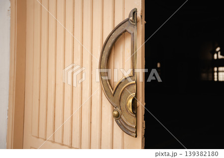 Wooden mosque entrance door with ornate brass door handle partially open showing dark interior space. Islamic architecture entrance detail 139382180