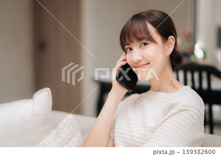 Happy young asian woman relaxing on comfortable couch with bright smile while holding mobile smartphone for phone call inside cozy living room enjoying cheerful conversation Happy young asian woman relaxing on comfortable couch with bright smile while holding mobile smartphone for phone call inside cozy living room enjoying cheerful conversation 139382600
