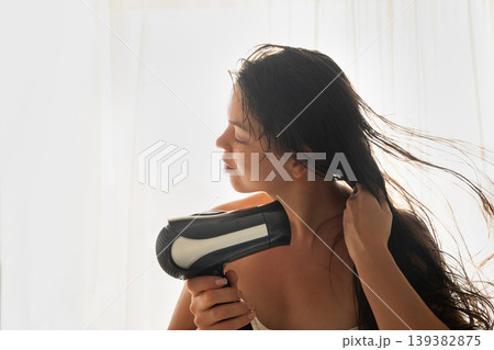 Attractive woman drying long hair with hairdryer in soft light, beauty haircare routine at home, female model with natural skin and relaxed pose, wellness and personal care concept Attractive woman drying long hair with hairdryer in soft light, beauty haircare routine at home, female model with natural skin and relaxed pose, wellness and personal care concept 139382875