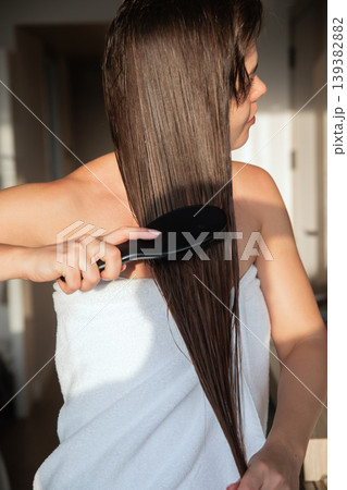 Beauty woman combing long straight wet hair with brush in soft sunlight, beautiful female model showing smooth texture and healthy shine, haircare routine and wellness lifestyle concept 139382882