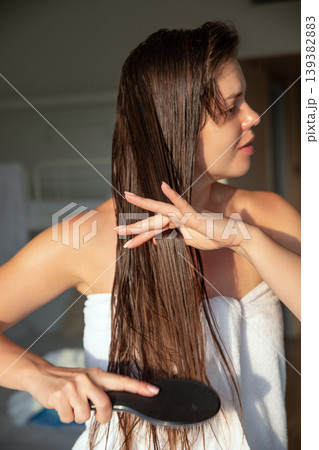 Pretty woman brushing long damp hair in sunlight, beauty haircare routine with smooth strands, female model with natural skin and relaxed posture, healthy lifestyle and grooming concept 139382883