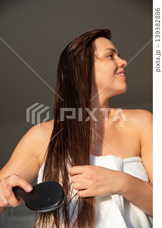 Female model brushing long wet hair with smooth motion in sunlight, beauty haircare routine at home, attractive woman with healthy shine and natural skin, wellness lifestyle concept 139382886