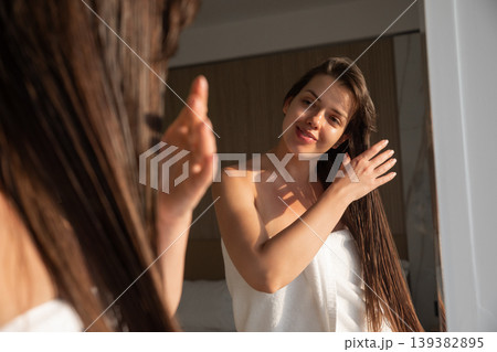 Beautiful woman touching long wet hair in mirror reflection soft morning light healthy shiny hair beauty routine portrait 139382895