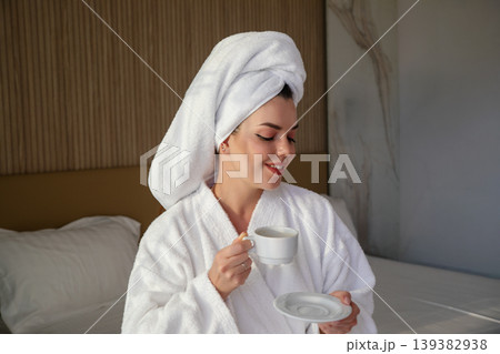 Woman enjoys coffee while wearing a robe and towel in a hotel room during morning hours 139382938