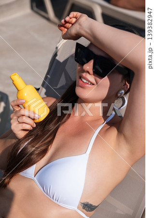 Woman relaxes by the pool while applying sunscreen during a sunny day at a resort Woman relaxes by the pool while applying sunscreen during a sunny day at a resort 139382947