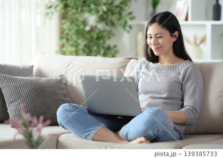 Satisfied asian woman using personal computer sitting at home Satisfied asian woman using personal computer sitting at home 139385733