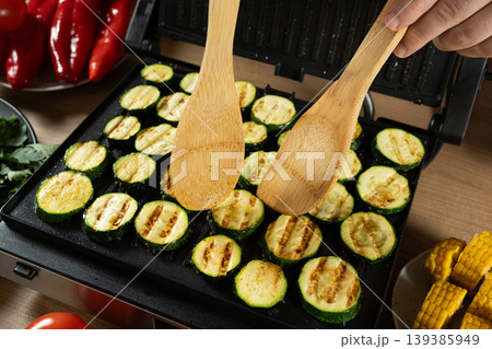Flipping Grilled Zucchini Slices with Wooden Spatulas on Electric Grill Flipping Grilled Zucchini Slices with Wooden Spatulas on Electric Grill 139385949